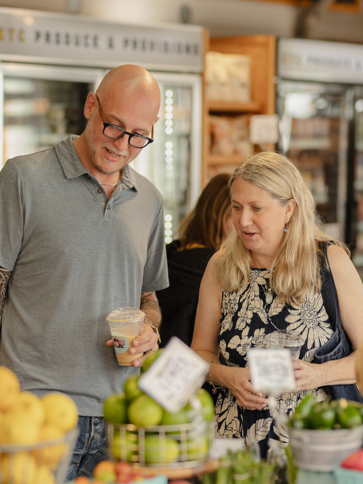 Two shoppers talking together inside a specialty market, refrigerated cases behind them.