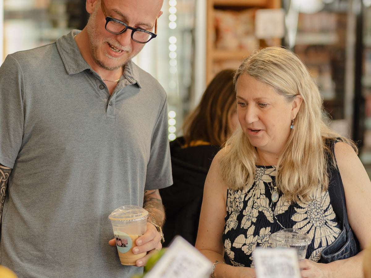Two shoppers talking together inside a specialty market, refrigerated cases behind them.