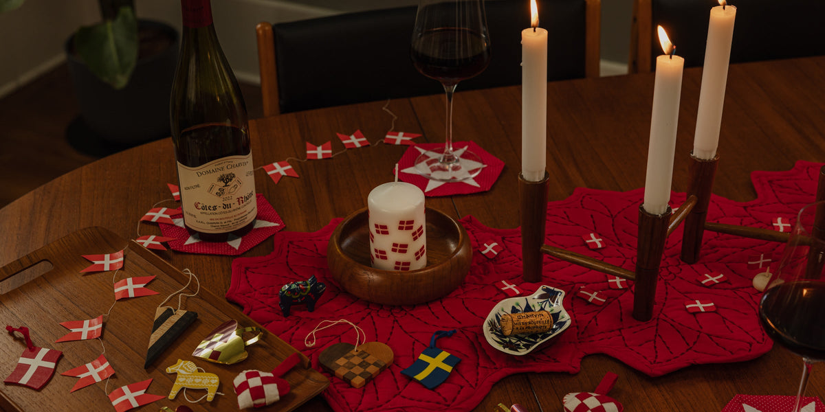 A candlelit Christmas table with a kalenderlys in a teak bowl on a red runner