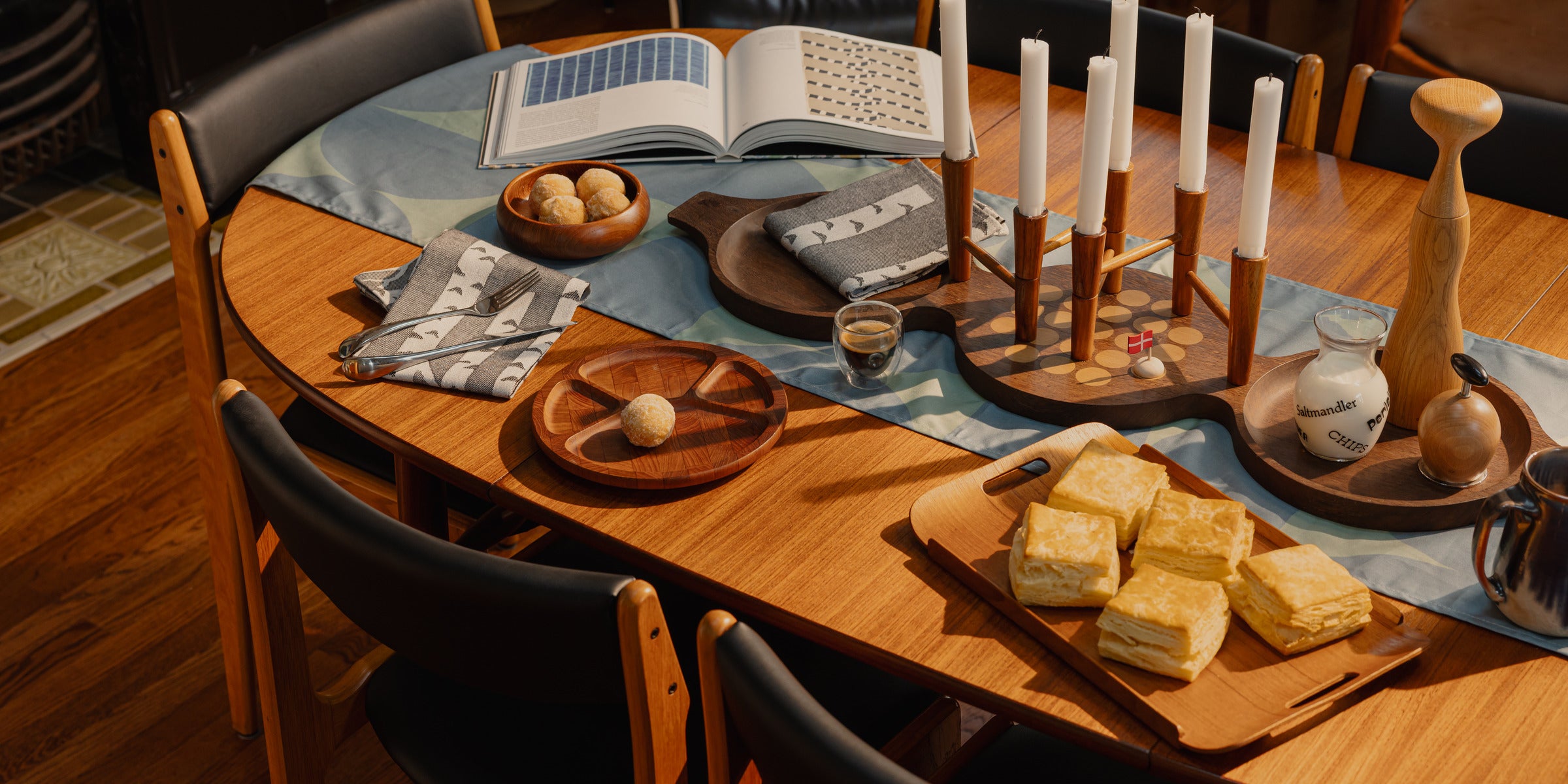 A Danish teak dining table set for coffee: candelabrum, open book, biscuits on a tray