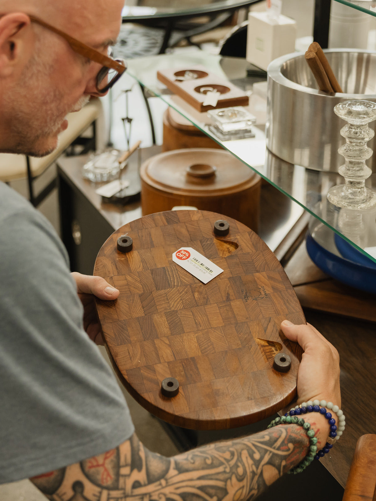 A shopper holding a round teak end-grain cutting board marked 30% off at a vintage shop.
