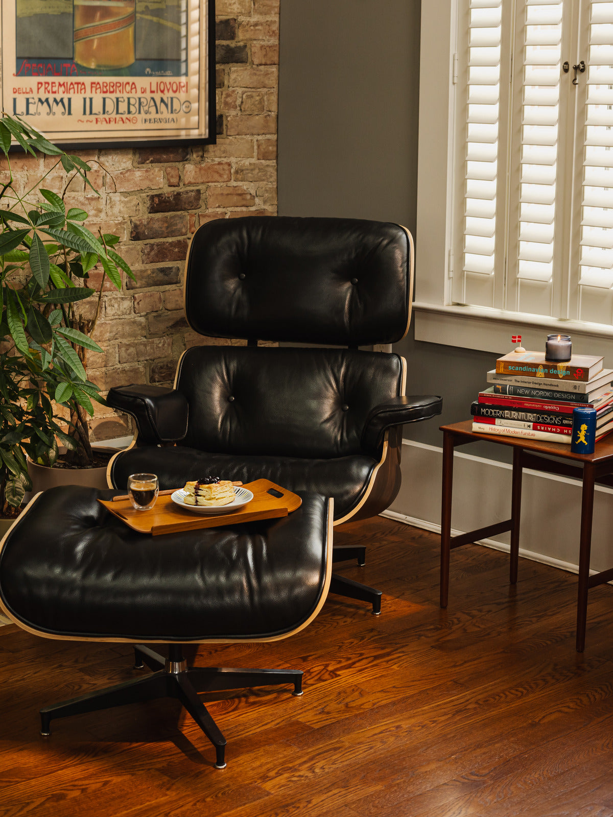 A living room corner with a black leather lounge chair, a stack of design books on a side table, and a carved wooden sculpture.